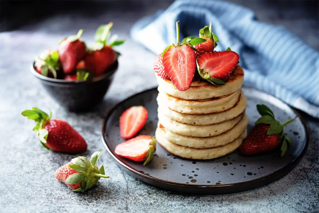 Mehrere Erdbeer-Pancakes auf einem dunklen Teller.